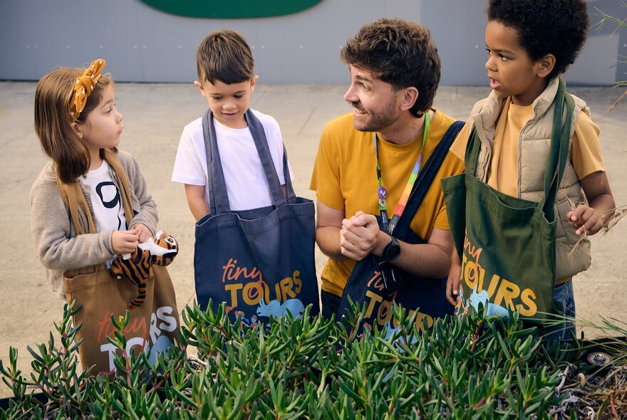 An instructor bobbing down to talk to three small children all wearing coloured aprons.