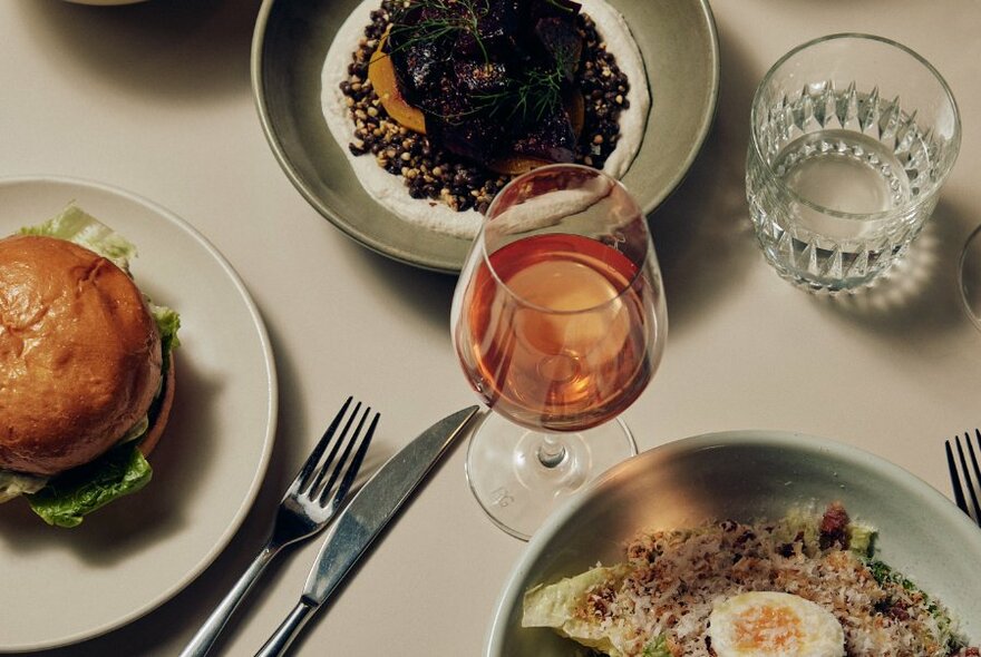 A restaurant table with cutlery, glasses and various dishes including a hamburger.