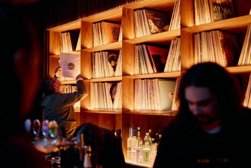 An illuminated wall of vinyl records in a dimly-lit bar setting.