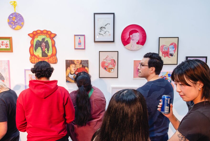 An exhibition of contemporary wall-based artworks in a gallery space, with people in the space looking at the art.