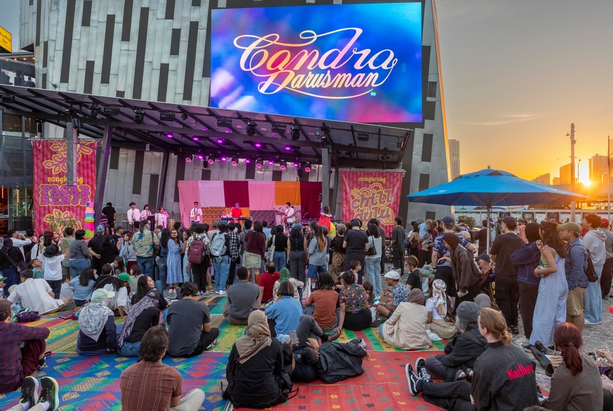 People sitting down in Federation Square at sunset. 