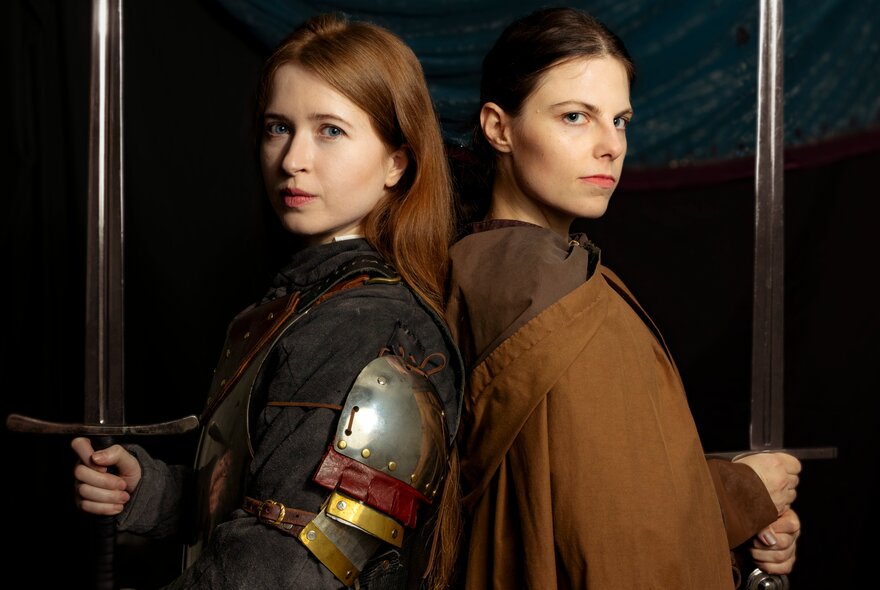 Two women dressed in medieval costumes standing back-to-back.