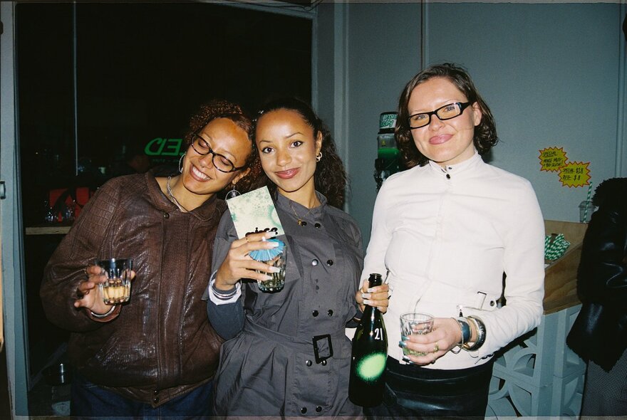 Three women posing for a photo with drinks in their hands.