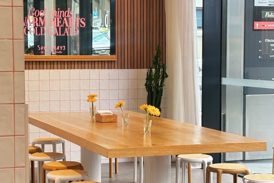 The modern, minimalist interior or an ice cream shop with a large wooden table and wooden stools.