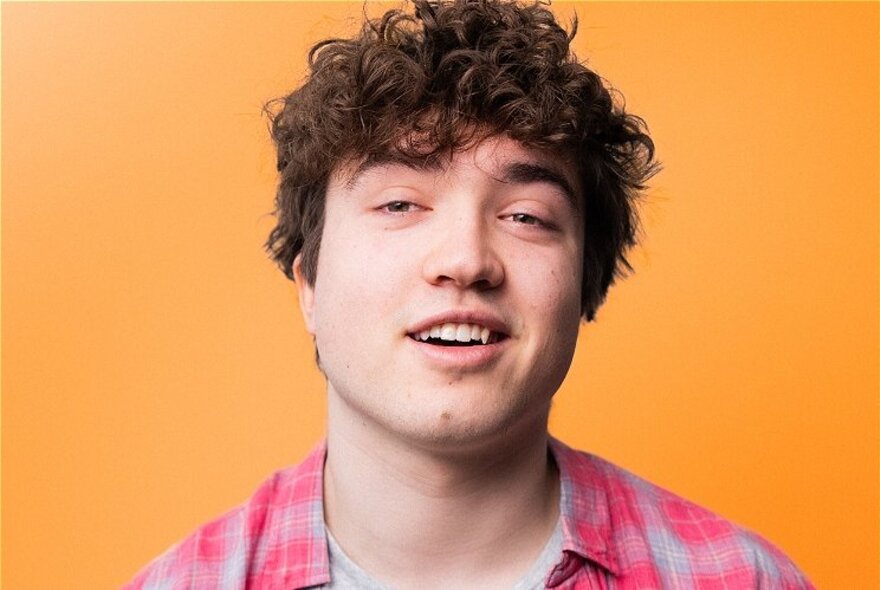 A man with scruffy hair cracking a lazy smile against an orange background. 