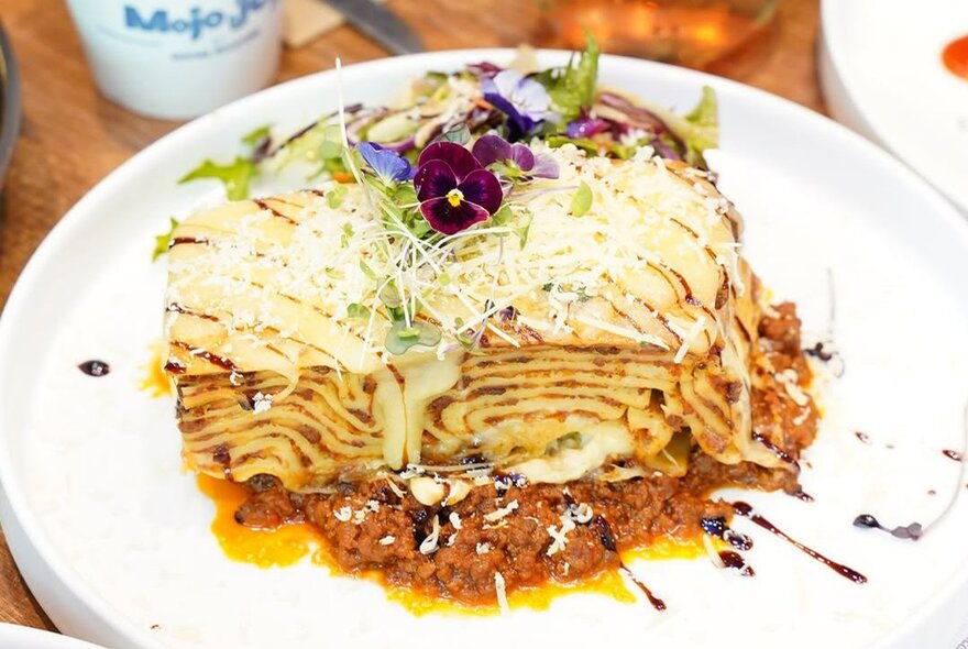 A plate of lasagne with edible flowers as garnish.