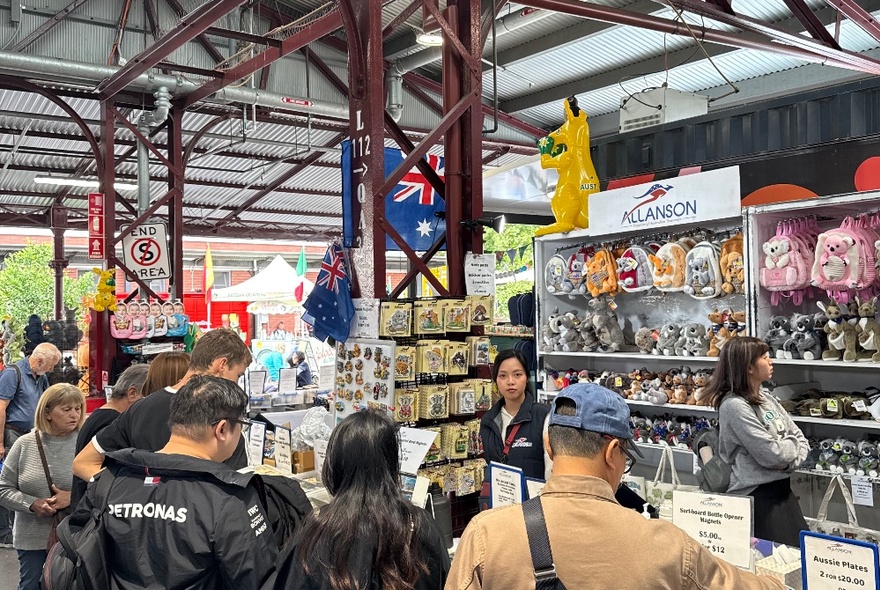 A stall at Queen Victoria Market filled with Australian souvenirs and other products, with shoppers browsing the display.