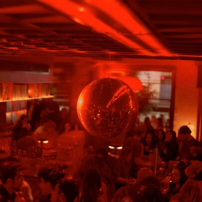 Looking down at the bar counter at LB's Record Bar, with people drinking and socialising, under a large mirror ball, with warm and atmospheric reddish lighting.