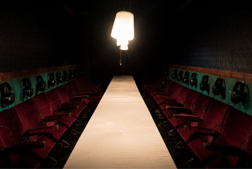 Two rows of seats facing each other, with headphones dangling above them, either side of a central illuminated aisle.