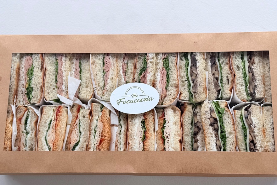 A box of catered halved sandwiches with a label on the box. 