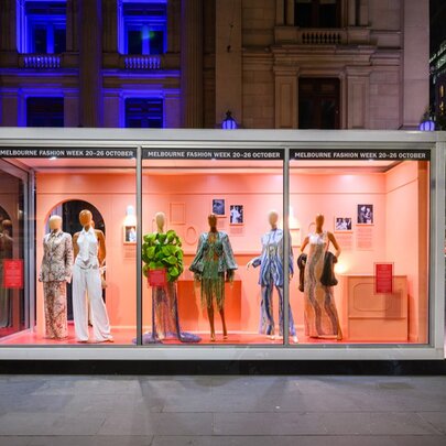 A Melbourne Fashion Week outdoor fashion capsule installation of fashion mannequins in a large glass rectangular case, displayed in a public space.