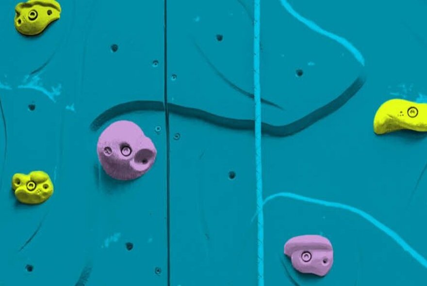 An illustration of a climbing wall; the flat wall is an aqua blue colour and the foot and hand holds are purple and yellow.
