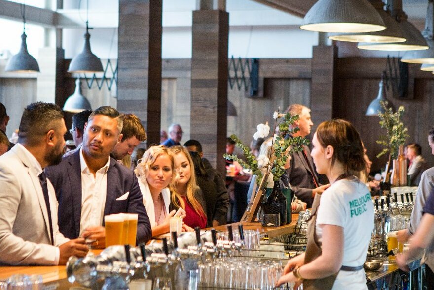 Patrons lined up at a bar waiting to order from the bar staff.