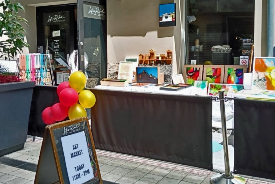 Trestle table stalls set up outside the Life's Too Short bar, displaying assorted arts and crafts and other items for sale.