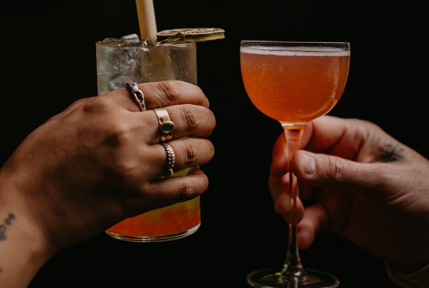 Two people clinking glasses of different cocktails in a toast, 