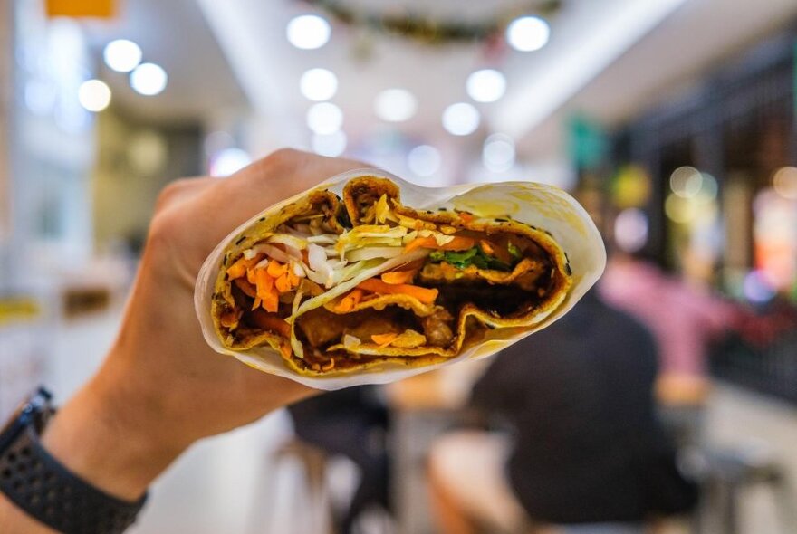 Chinese crepe filled with vegetables being held in hand