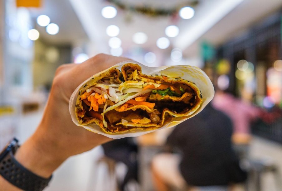Chinese crepe filled with vegetables being held in hand