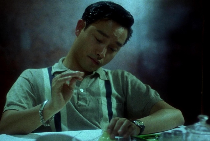 A still from the movie, Days of Being Wild, showing a young man in a 60's style polo shirt, seated at a table.