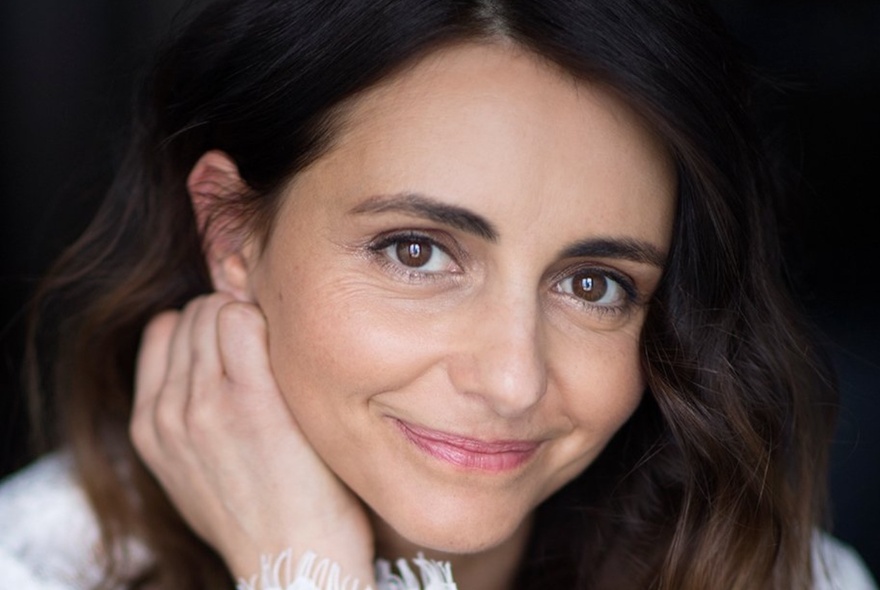 Actress Pia Miranda, her hand resting under her chin with a slight smile on her face.