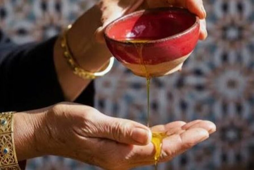 A woman pouring oil on her hand from a small red pottery bowl. 