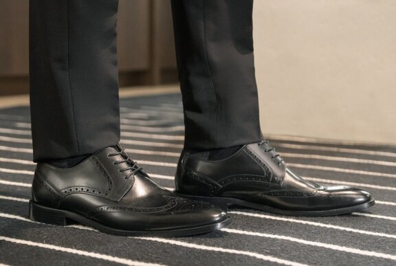A close-up of black pants and black leather shoes.