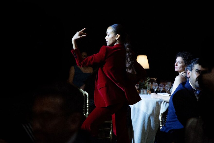 A still from the movie Emilia Pérez with a woman in a red velvet soon performs in front of seated restaurant patrons.