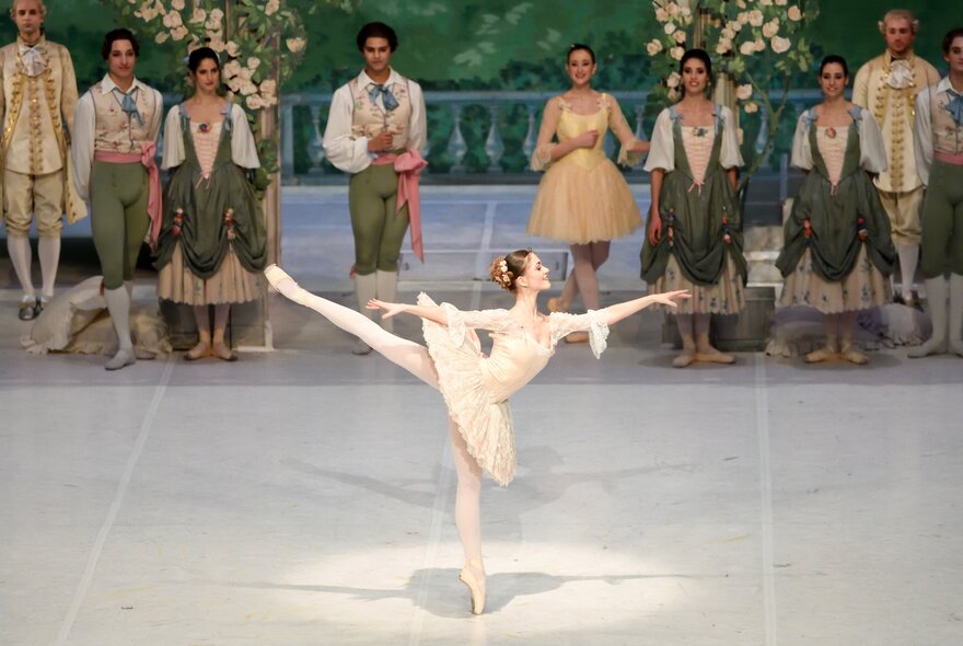 A ballerina performs a pose with one leg in the air as the troupe looks on. 