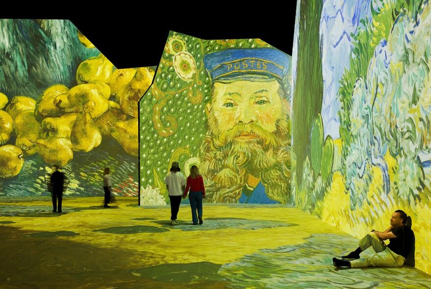 People walking around a very large exhibition space with Vincent van Gogh's paintings digitally projected on all the wall and floor spaces.