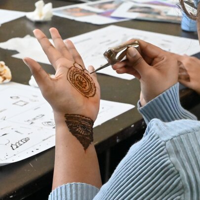 A person applying henna art to their hand using a fine applicator cone as part of a henna art workshop.