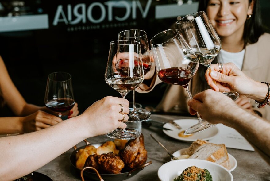 Several people raising their glasses of wine for a celebratory toast over a table of food.