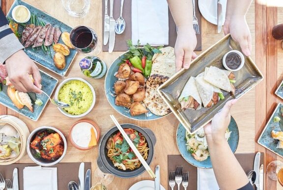 Looking down at a table filled with different sized plates of food, with hands reaching across with forks.