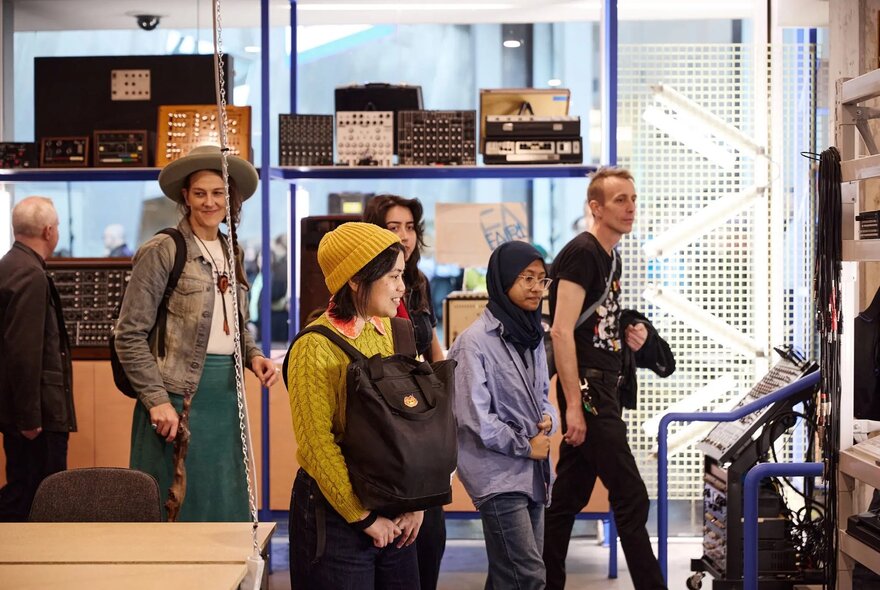 Visitors on a tour at the Melbourne Electronic Sound Studio with electronic instruments on display on shelves. 