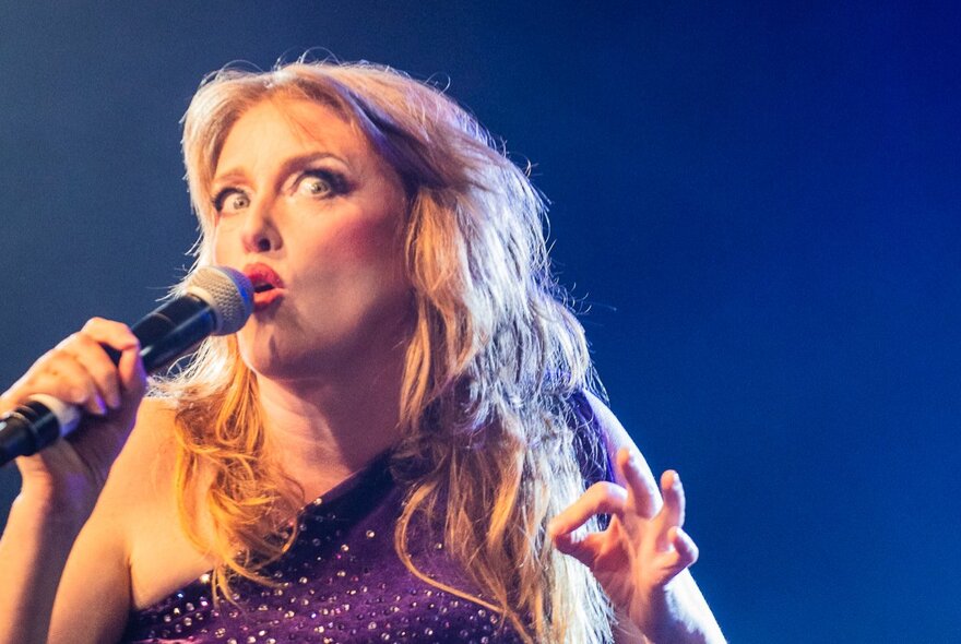 Performer Geraldine Quinn singing into a microphone she is holding.
