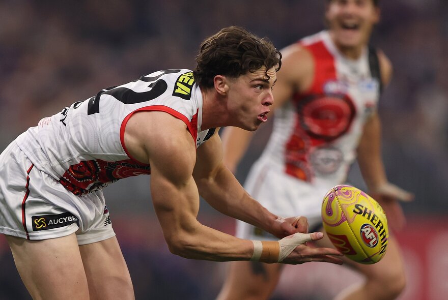 A St Kilda AFL football player handballing the ball during a match.