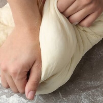 Hands kneading bread dough on a floured surface.