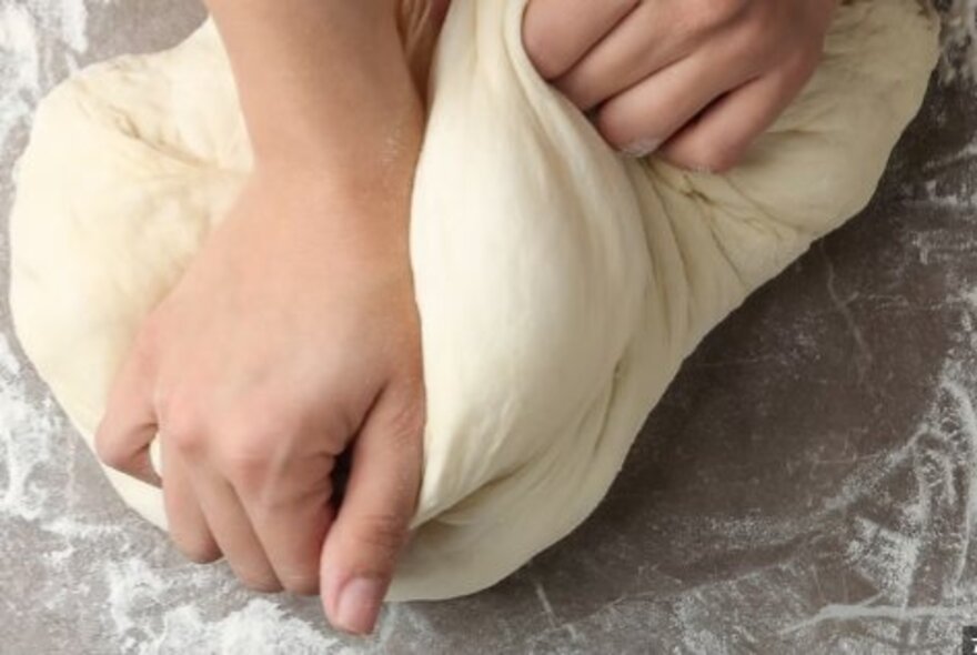 Hands kneading bread dough on a floured surface.