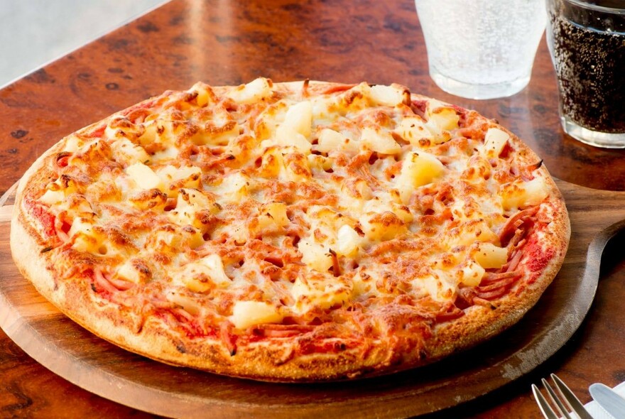 Wooden table with a pizza on a wooden platter with drinks.