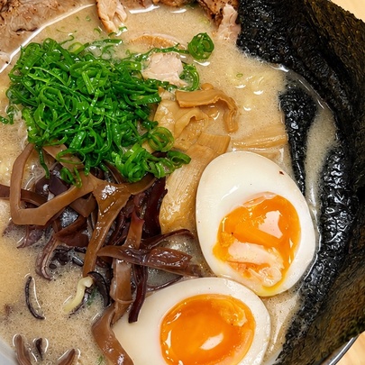 A bowl of tonkotsu ramen, featuring a creamy, broth topped with pork, a soft-boiled egg with a jammy yolk, mushrooms, and nori seaweed.