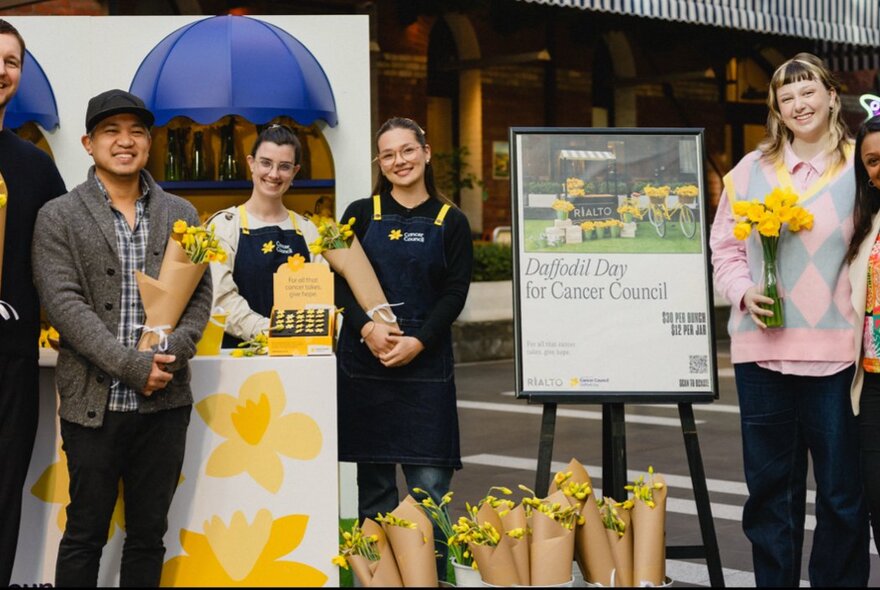 People smiling and holding bunches of daffodils wrapped in brown paper.