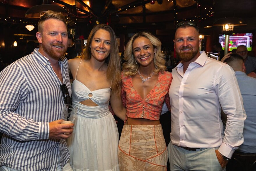 Four people posing with arms around each other for a group shot in a pub.