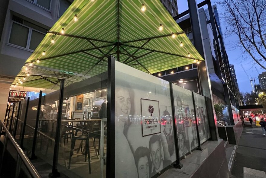 Square green umbrella with lights, over outdoor seating at a cafe.