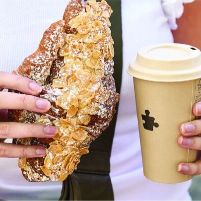 Tight shoyt of a hands holding a large almond croissant and a large takeaway coffee cup. 