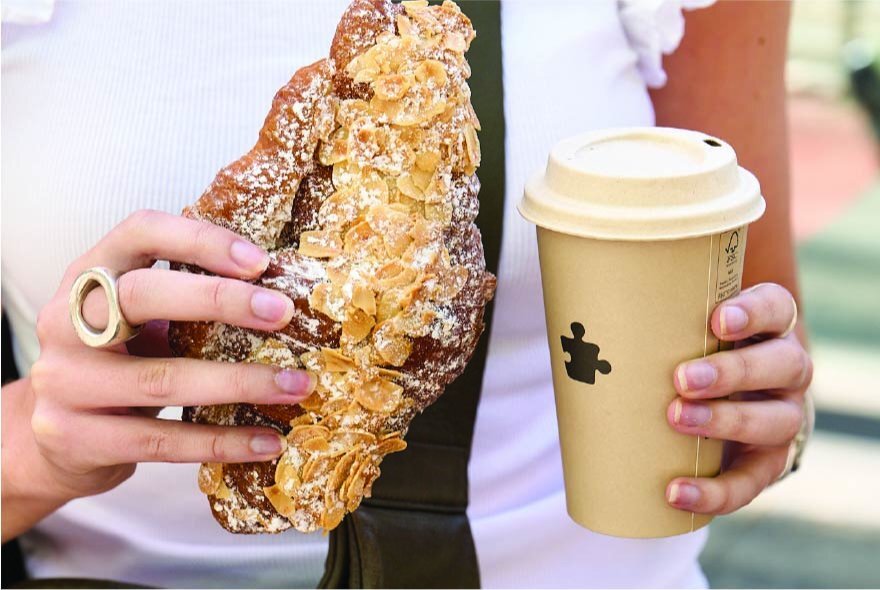Tight shoyt of a hands holding a large almond croissant and a large takeaway coffee cup. 