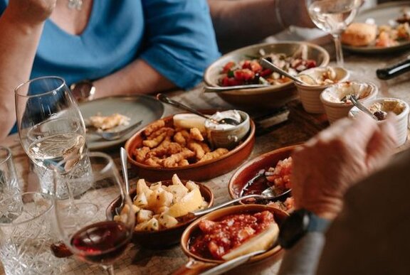 People seated at a restaurant table with platters of food and glasses of wine before them.
