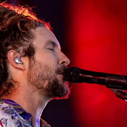 Profile of the head of singer Jeremy Loops, his hair is piled on top of his head in a loose bun, his eyes are closed and he sings into a microphone.