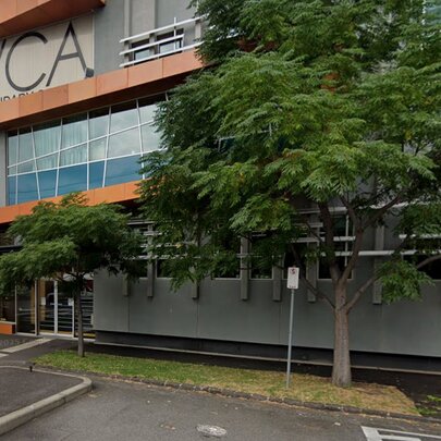 The exterior of the Victorian College of Arts building with a level crossing and trees out the front. 