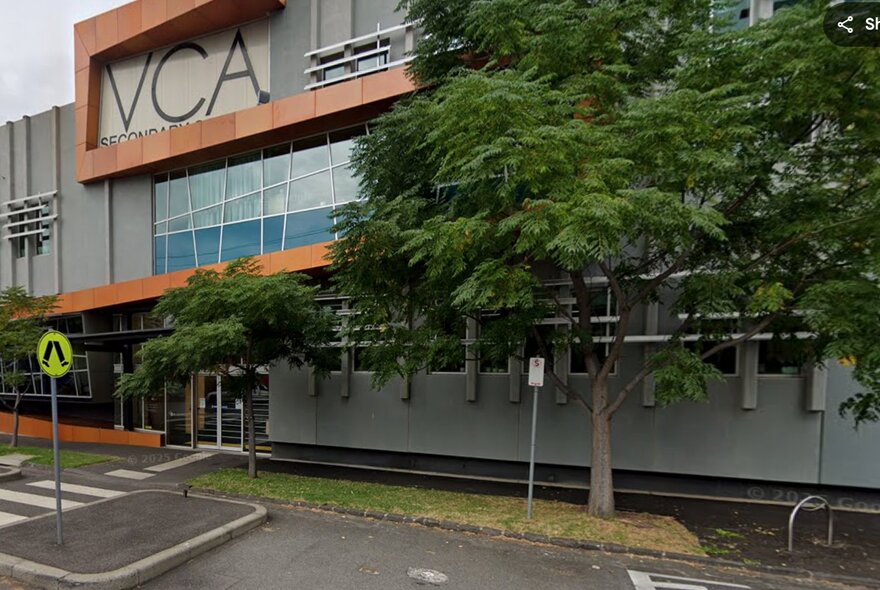 The exterior of the Victorian College of Arts building with a level crossing and trees out the front. 