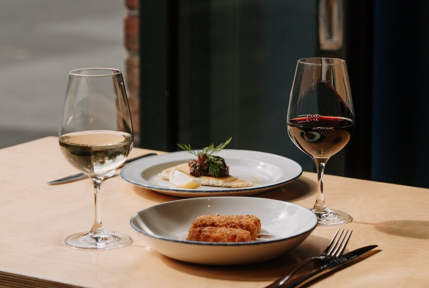 A table set with two elegant small dishes and two glasses of wine. 