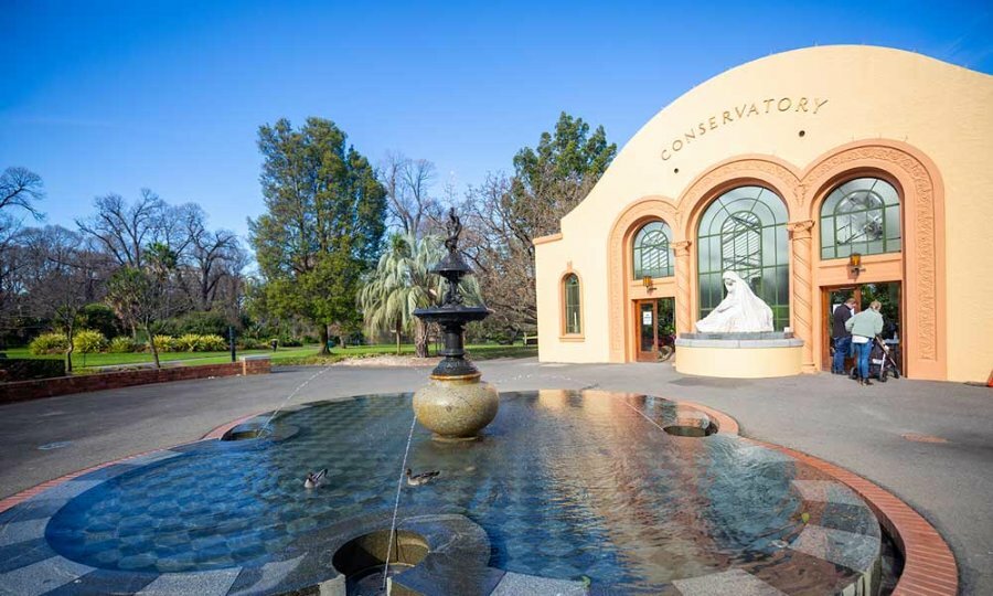 A bronze fountain in front of a large conservatory