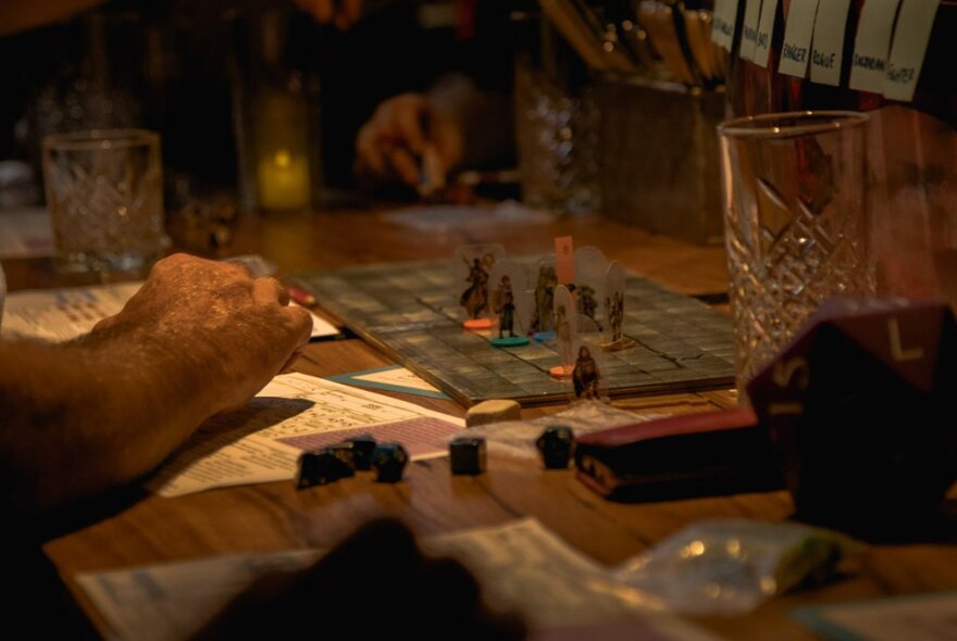 Hands visible around a dimly-lit table where people are playing a board game. 